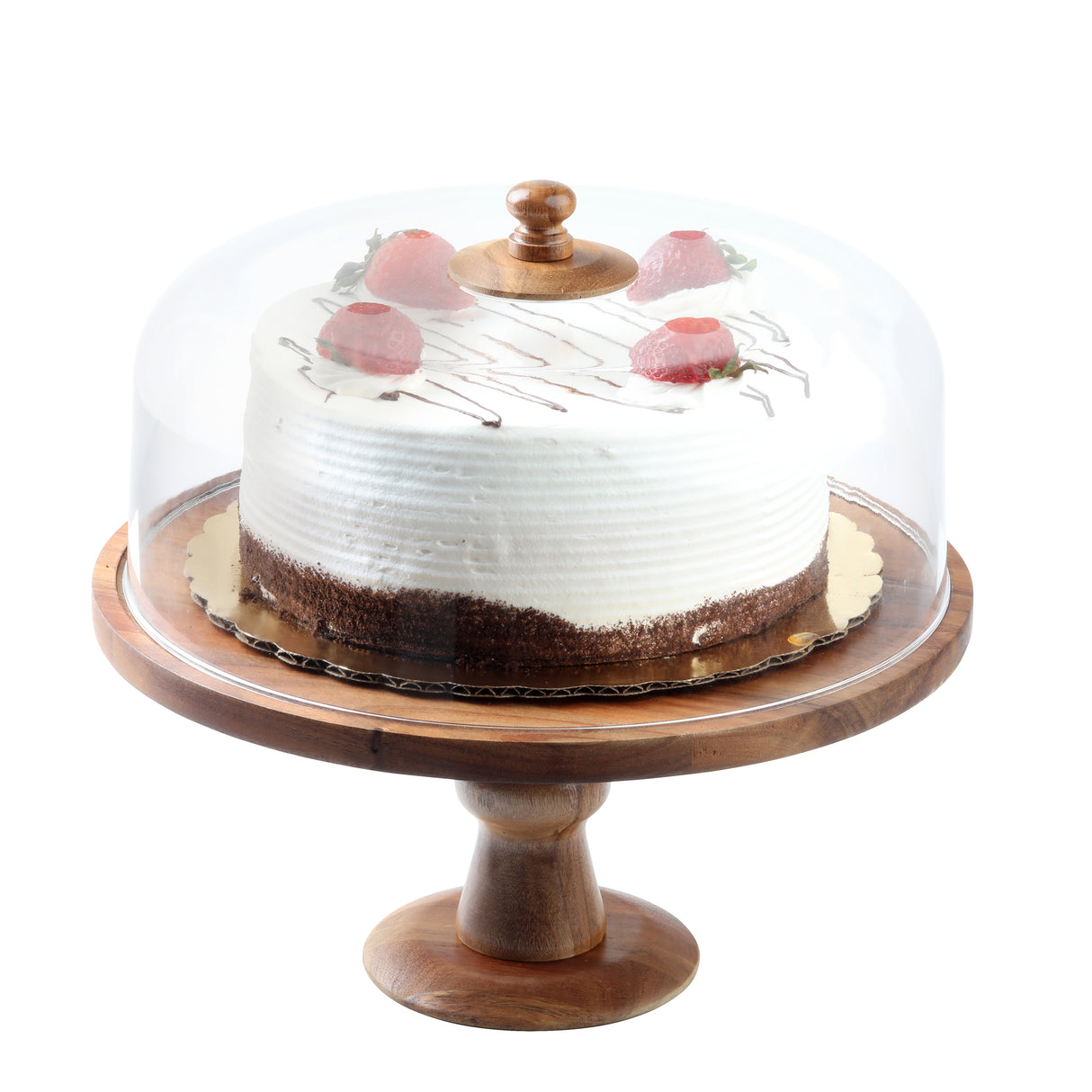 A round, frosted cake with chocolate shavings and pink fruit pieces sits on a wooden cake stand, covered by an Acacia Cake Dome with a clear glass lid and wooden knob. The cake features white swirled frosting over a chocolate base layer.