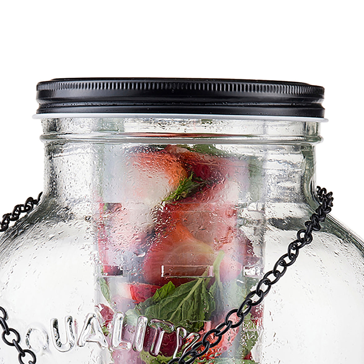 A close-up of a large TableCraft beverage dispenser with a black screw-on lid and metal chain. Inside, fresh strawberries, ice cubes, and mint leaves are visible through condensation on the cold glass surface.