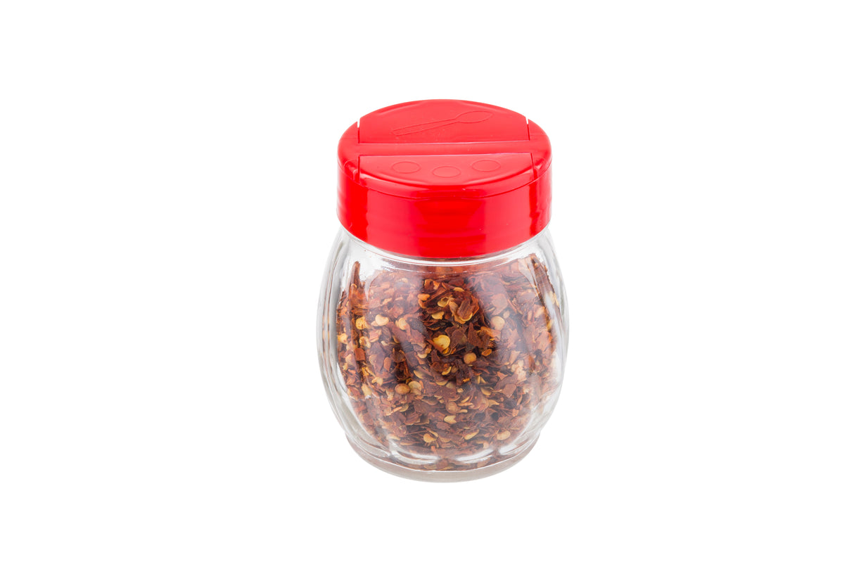 A clear glass shaker jar filled with red chili flakes, topped with a bright red flip top plastic lid featuring two openings for sprinkling or pouring. The jar is isolated on a white background.