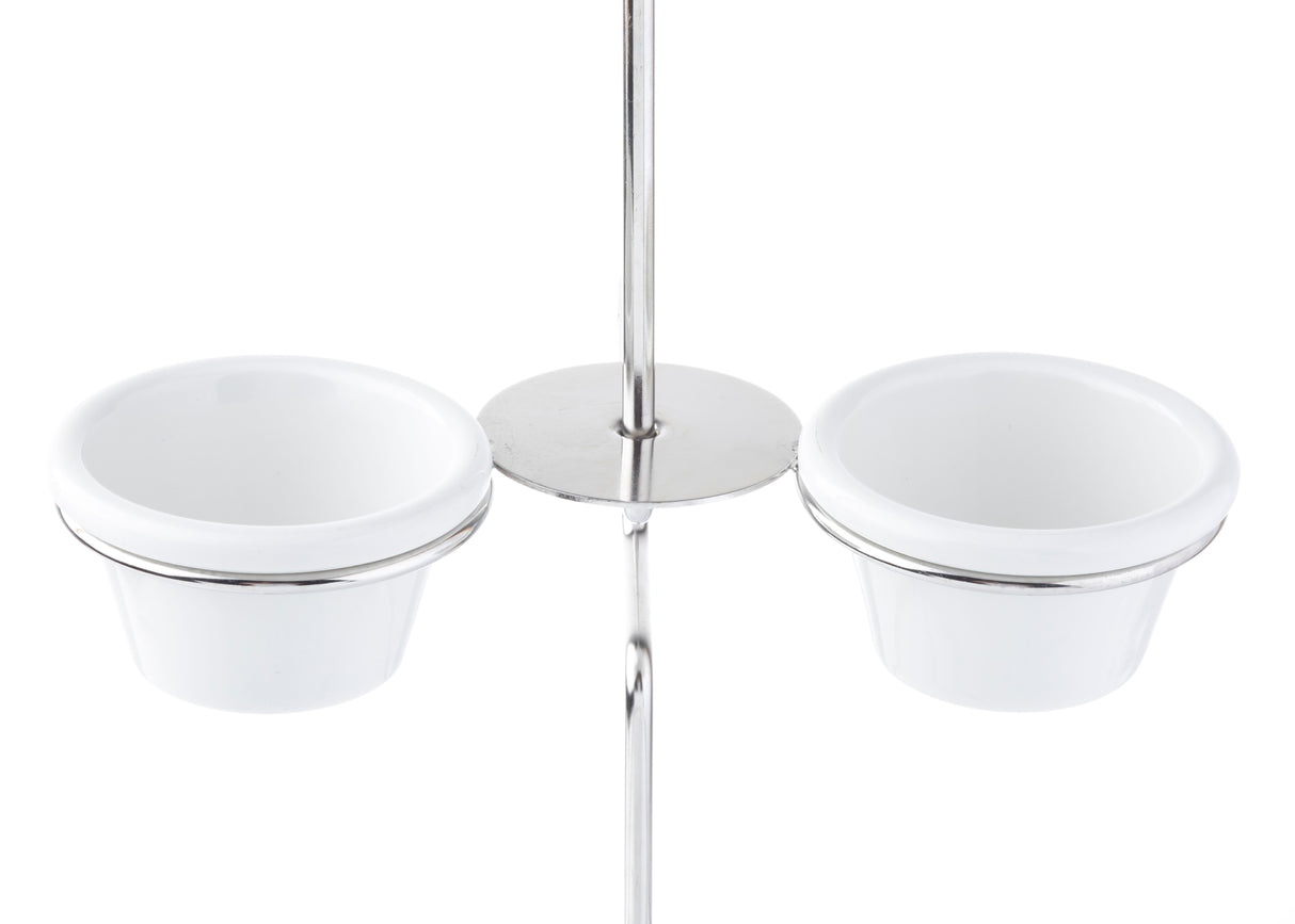 Two white ceramic cups with metal rims are held in a shiny stainless steel stand with a central pole and round base. The setup, reminiscent of ramekin holders, is viewed from above on a completely white background.