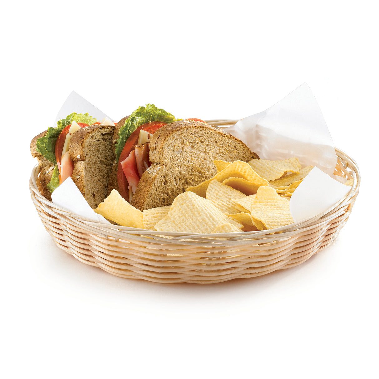 A hand-woven basket lined with white paper holds a sandwich made with whole grain bread, lettuce, tomato, and other fillings, alongside wavy potato chips. The food is arranged neatly against a white background.