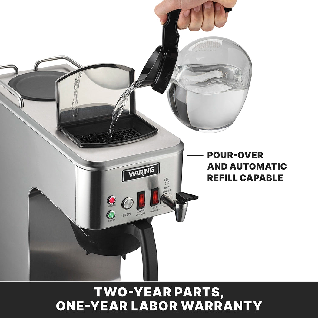 A hand pours water from a clear pitcher into the top of a stainless steel coffee brewer. The machine, an automatic coffee brewer, features indicator lights, a spout, and text highlighting pour-over and automatic refill capability. Warranty details below.