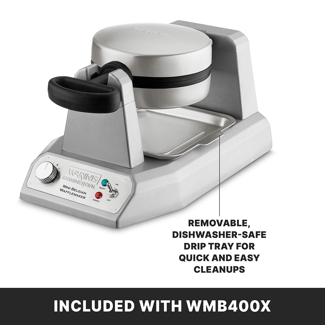 A silver heavy duty waffle maker with a black handle sits on a counter. It features non-stick waffle plates, a control knob, and an indicator light. A removable, dishwasher-safe drip tray is shown beneath it. Banner below reads: INCLUDED WITH WMB400X.