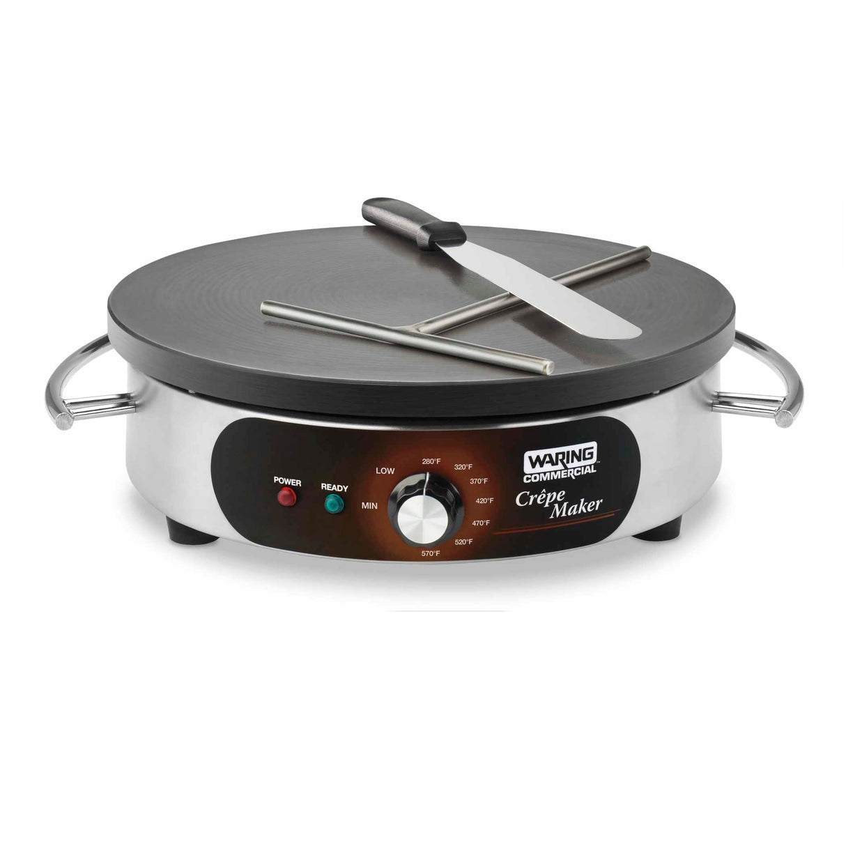 A stainless steel Waring commercial crepe maker with a round cast iron cook surface, front control knob, adjustable thermostat, indicator lights, side handles, a wooden crepe spreader, and a metal spatula resting on top. Temperature settings show on the front panel.