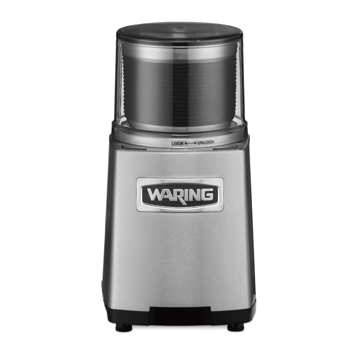The Waring WSG60E Commercial Spice Grinder features a stainless steel cylindrical build, clear plastic lid with lock/unlock markings, and black accents. Designed for international use, its sturdy base with four short legs ensures stability on any surface.