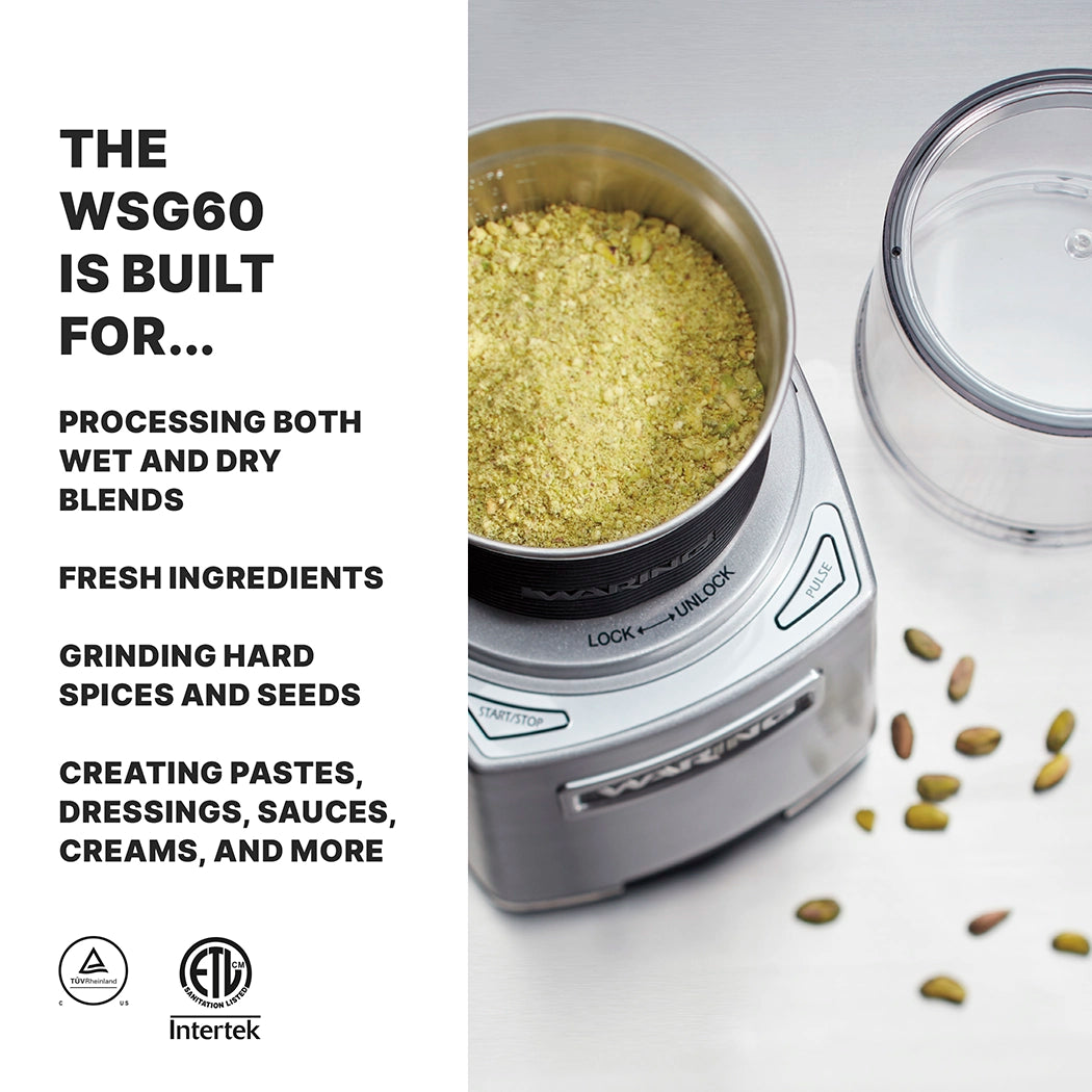 A silver Commercial Spice Grinder filled with greenish-yellow powder sits on a white surface beside its clear lid and scattered cardamom pods. Text on the left reads: "The Waring WSG60E is built for international use, processing both wet and dry blends, and more.
