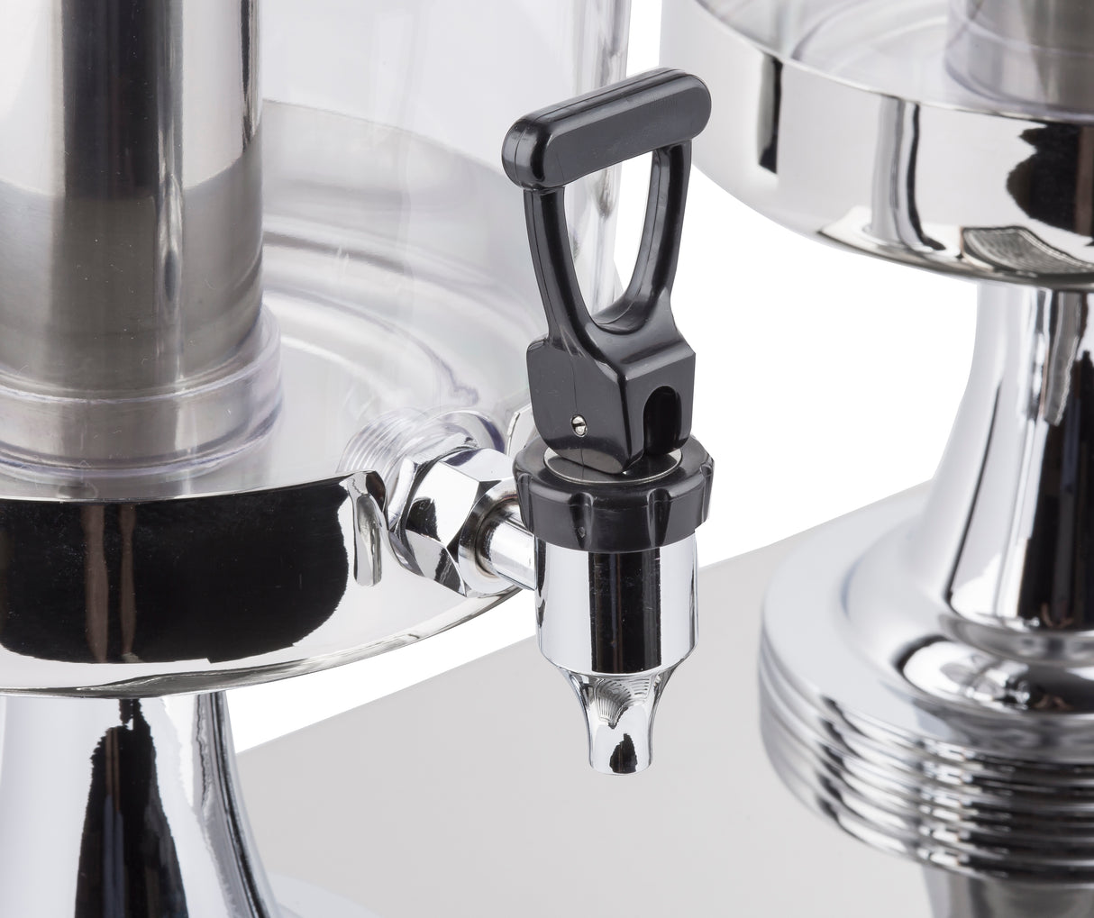 Close-up of a stainless steel and black plastic beverage dispenser spigot attached to a clear container. The handle is upright, reflective surfaces capture light, and another dispenser appears to the right against a white background.