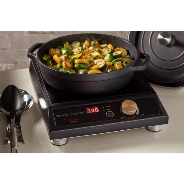 A black induction cooktop with a digital display reading 400 holds a round black pot filled with cooked mixed vegetables, including zucchini and yellow squash. Utensils and a pot lid sit nearby on a cream-colored countertop induction range.