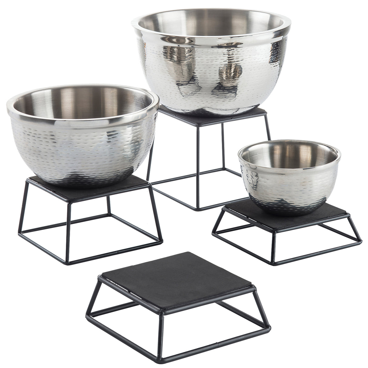 Four hammered metal bowls of varying sizes rest on black powder coated metal stands. One stand is empty, while the others hold shiny, textured stainless steel bowls. This TableCraft Products riser set elevates each bowl to a different height for striking display.