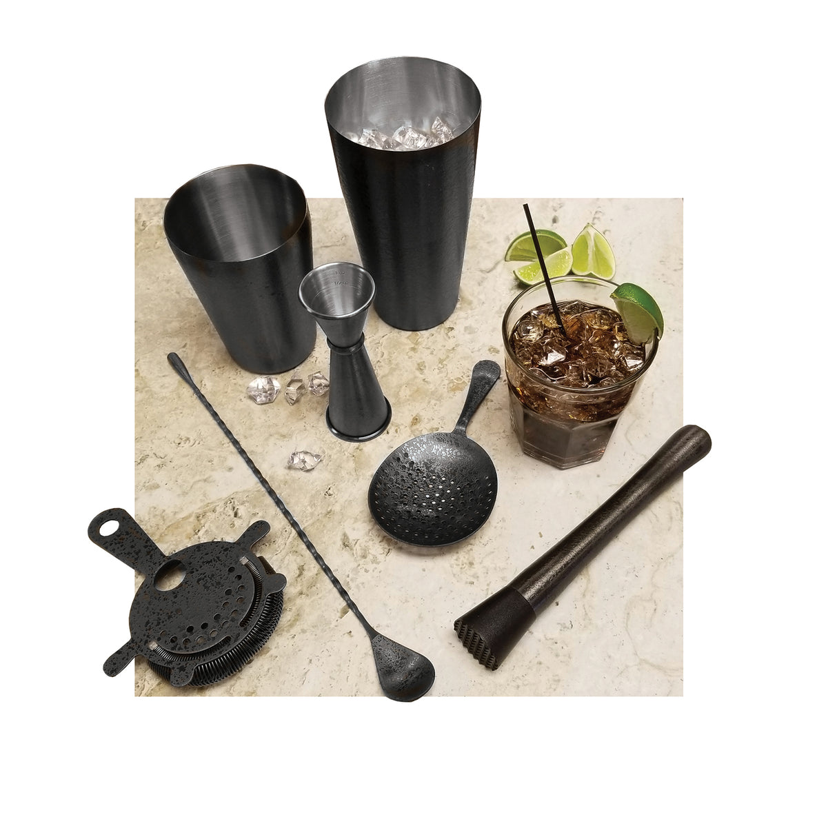 A marble countertop displays a Premium Barware Set: two stainless steel cocktail shakers, a jigger, muddler, strainer, long bar spoon, and a drink with ice, soda, lime wedges, and herbs. A few ice cubes are scattered on the surface.