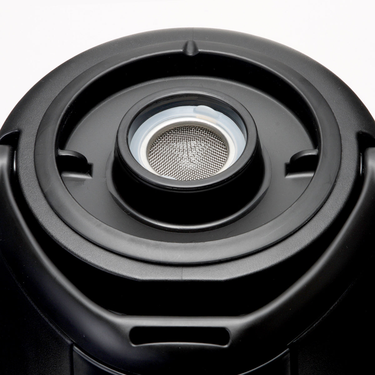 Close-up of a black circular appliance part, likely an insulated beverage dispenser lid, featuring a central metal mesh filter or strainer. The filter is surrounded by a white ring, with grooves and a handle on the outer black plastic surface.
