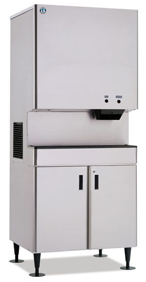 A large, industrial stainless steel ice machine with a boxy upper section for making ice and a lower cabinet with two doors for storage; the machine stands on an equipment stand with four sturdy black legs.