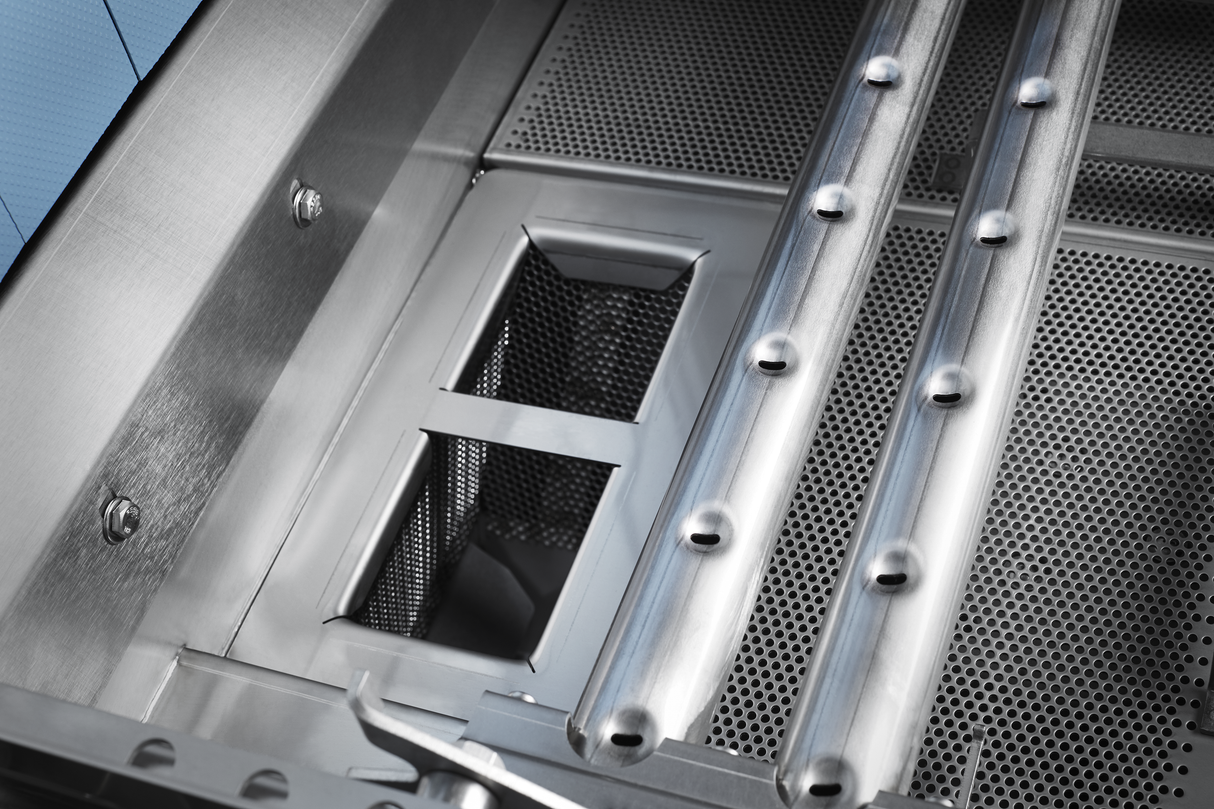 Close-up of a stainless steel grill interior showing perforated metal surfaces, rectangular compartments, and two tubular burners with evenly spaced ports—reminiscent of the precision seen in conveyor dishwasher designs with automatic soil removal.