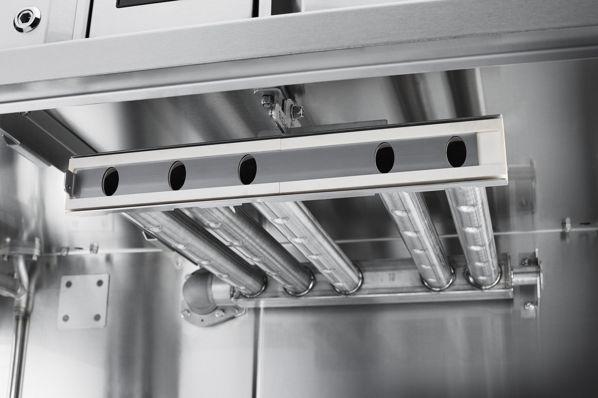A close-up view of a stainless steel industrial appliance interior shows four cylindrical metal pipes running parallel, connected to a rectangular component with five oval openings—ideal for conveyor dishwasher systems with automatic soil removal.