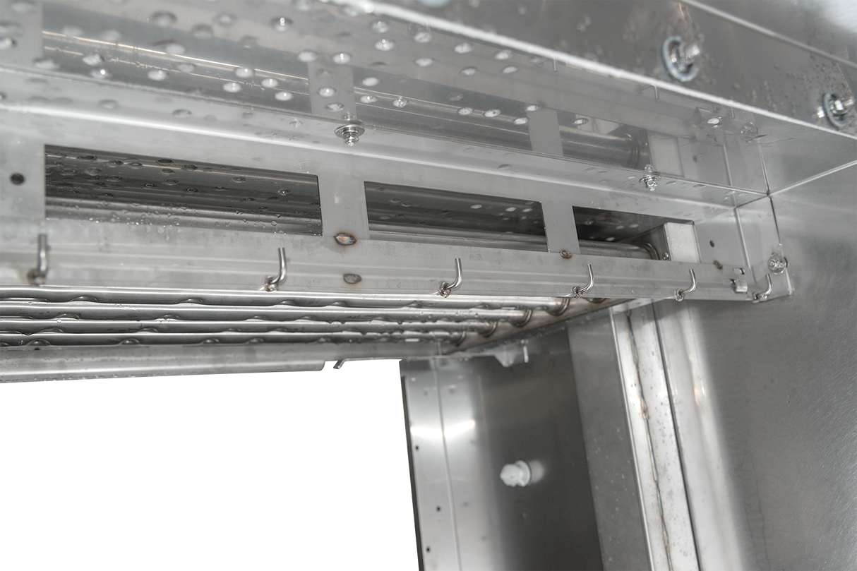 Close-up of the interior of a flight type dish machine, showing metal racks, hooks, and water jets. The clean, shiny surfaces and water droplets highlight its energy recovery features and industrial design.