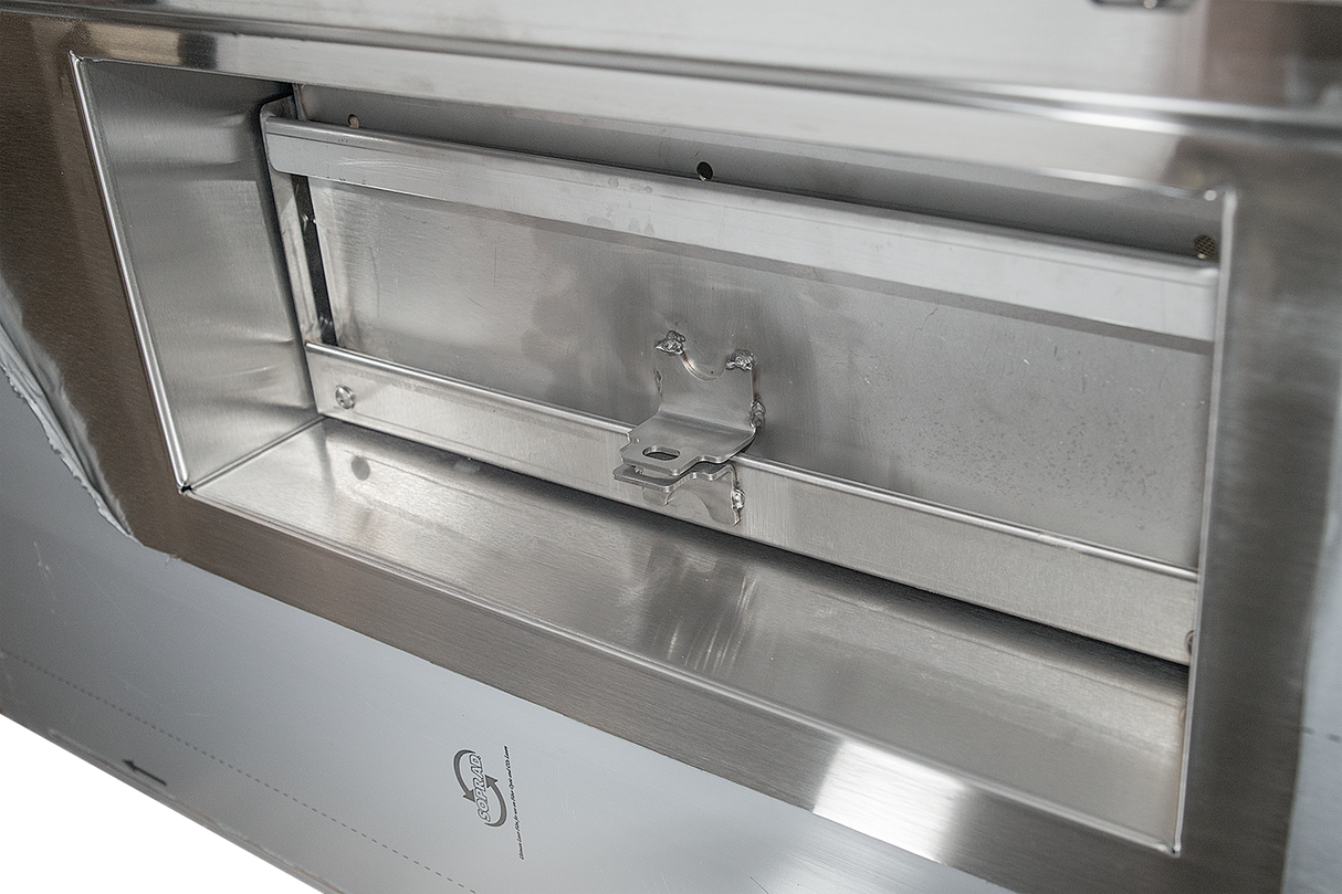 Close-up of a metallic mail slot or delivery box with a hinged flap and latch, set into a stainless steel surface from the low energy series. The rectangular opening has a reflective finish, minor scratches, and a small printed symbol below.