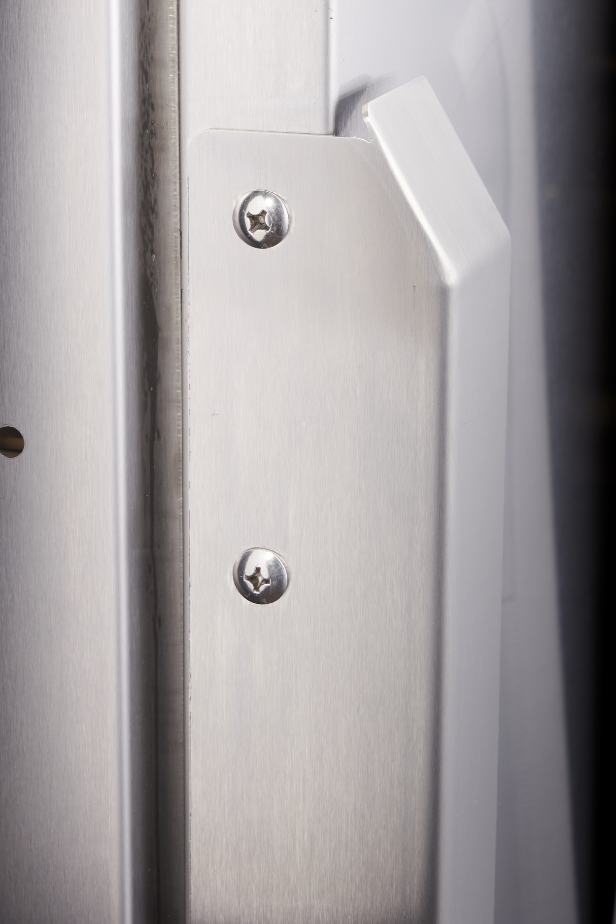Close-up of a brushed metal strike plate with two star-shaped screws, mounted on a door frame. The edge of a white door is visible on the right, and the plate covers the latch area—similar precision as found in a Hobart FT1000E flight type dish machine.