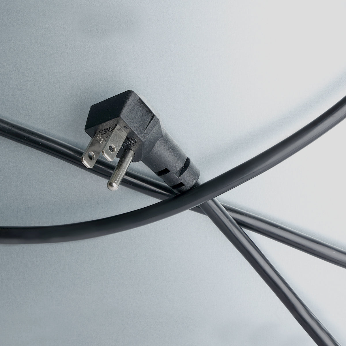 A black electrical plug with two metal prongs is attached to a cable that crosses another, forming an X shape on a smooth, light gray surface—like the minimalistic lines of an Empura refrigeration back bar cooler. The image is evenly lit.