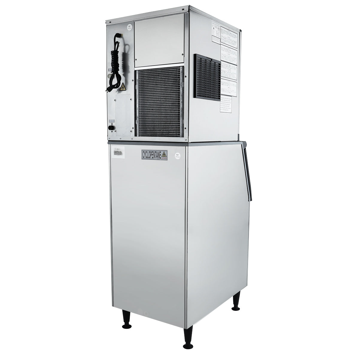 A cube-style ice maker with a silver metallic finish, standing on four black legs. The upper section has vents, a control panel, and coiled hose, while the lower commercial ice bin features a handle. Labels and instructions are visible on the side.