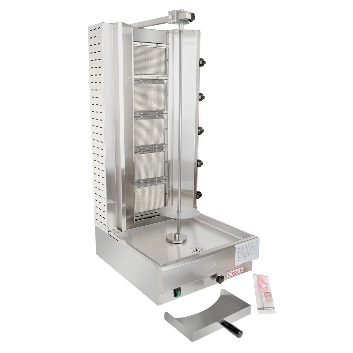 A stainless steel vertical broiler features rear heating elements, a central spit for meat, a drip tray below, and control knobs on the right. A large curved meat knife and a wrapped cleaning brush sit beside the base.