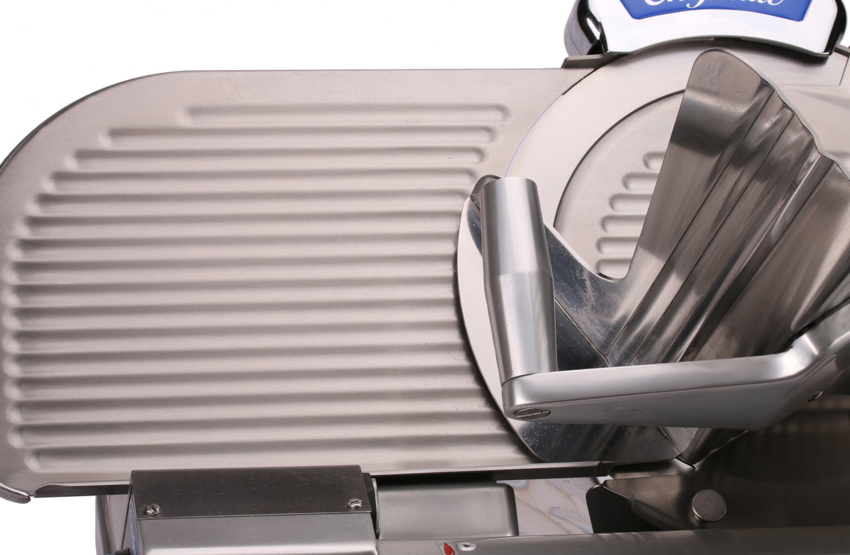 Close-up of a Chefmate Series 12 inch slicer, with a ribbed sliding tray on the left and an angled food holder on the right. The compact slicer features clean, industrial metallic surfaces and visible mechanical parts.