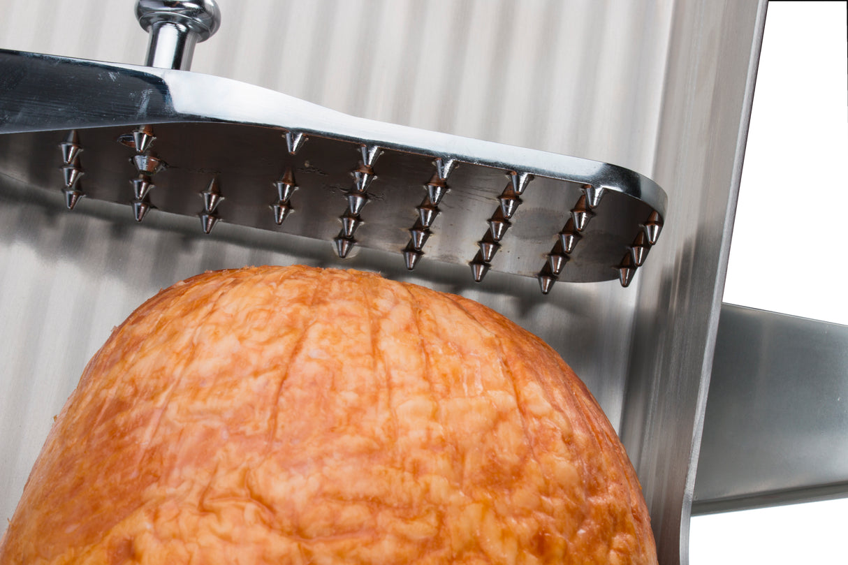 Close-up of a large piece of meat under a metal meat tenderizer with pyramid-shaped spikes. The Chefmate Series tool is poised above the meat, set against a ribbed metal surface and a vertical bar on the right.