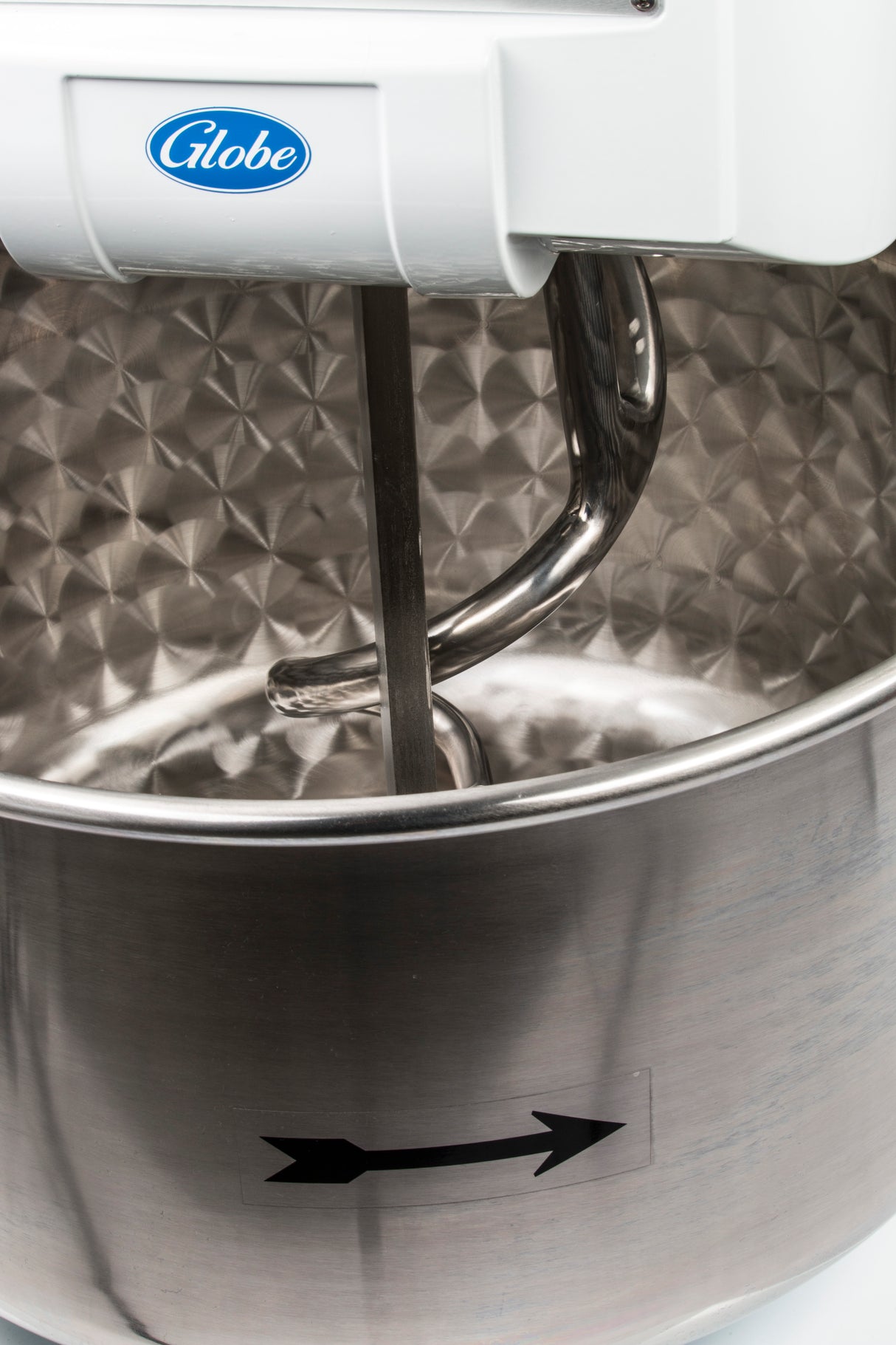 Close-up of a commercial spiral dough mixer with a Globe label, featuring a spiral dough hook inside a large, textured stainless steel bowl. A black arrow sticker on the bowl indicates its rotational direction; this model boasts 130 lbs capacity.