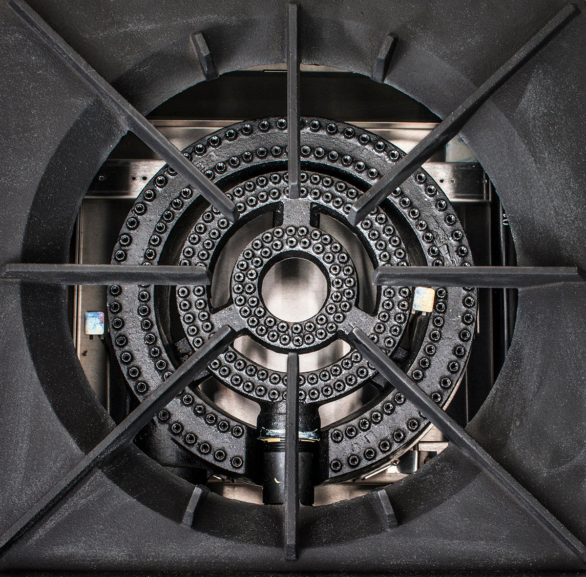 Close-up view of a Globe GSP18G stock pot range burner with concentric gas outlets. The heavy cast iron grate features thick crossbars forming an X, and the metallic surface shows slight texture and some visible screws.