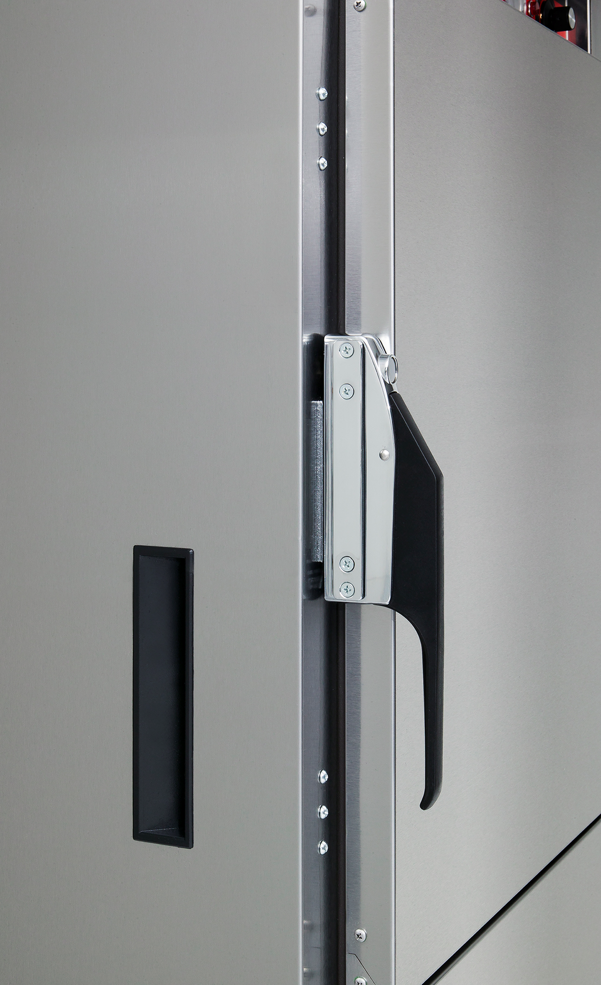 Close-up of a stainless steel cabinet door on a commercial mobile food cabinet, showing a black recessed handle on the left and a silver and black latch handle on the edge, secured with screws, with visible hinges and textured finish.