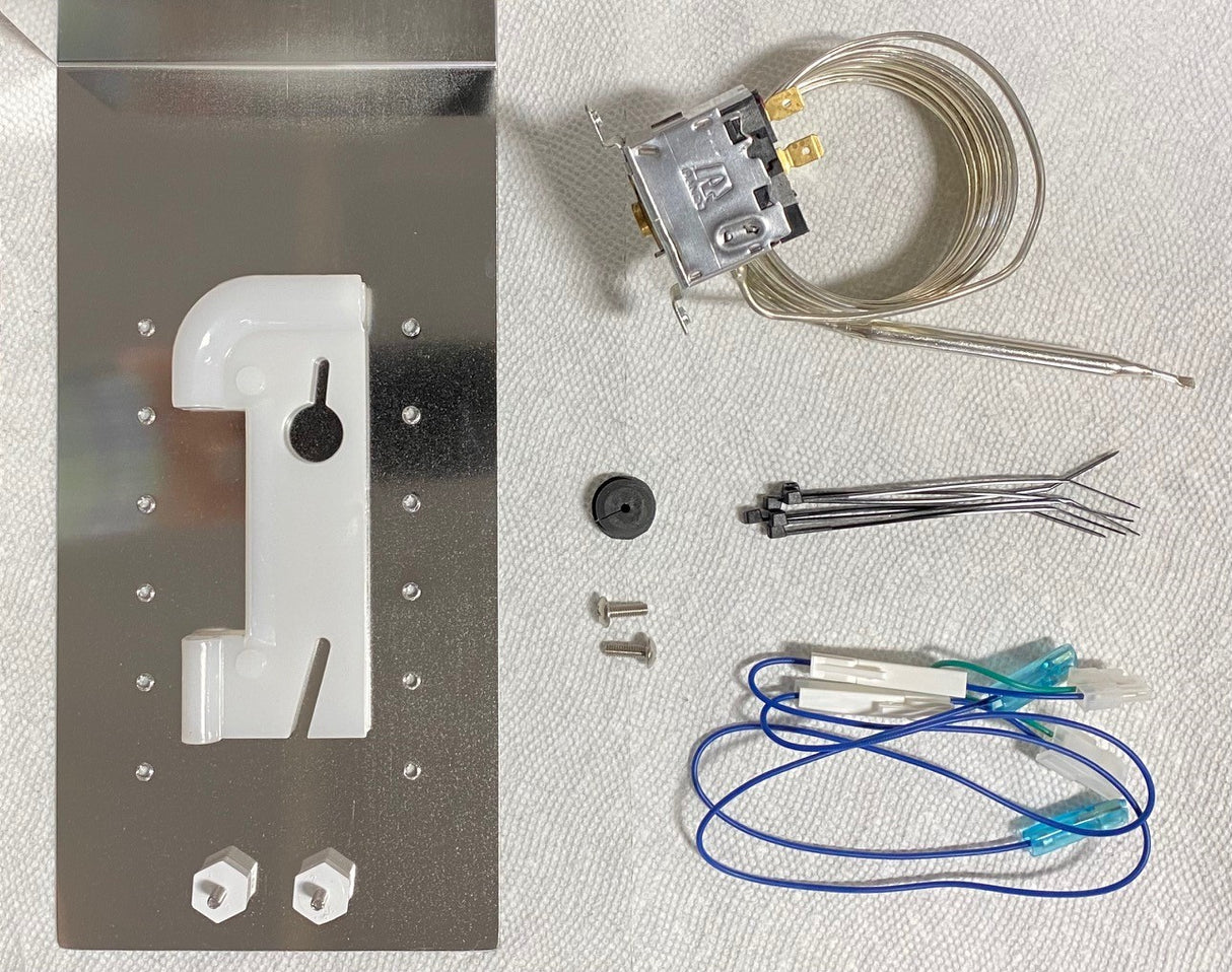 Various refrigerator thermostat replacement parts—including an FS9100 Bin Stat Kit, metal mounting plate, thermostat with probe, plastic bracket, screws, zip ties, and blue electrical wires—are displayed on a white textured surface.