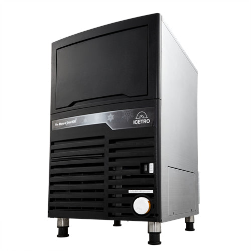 A commercial cube-style ice maker with a black front panel, ventilation grilles, and a small control panel. The “ICETRO” label is visible. This unit features a self-contained condenser and stands on four short legs with a modern, rectangular design.
