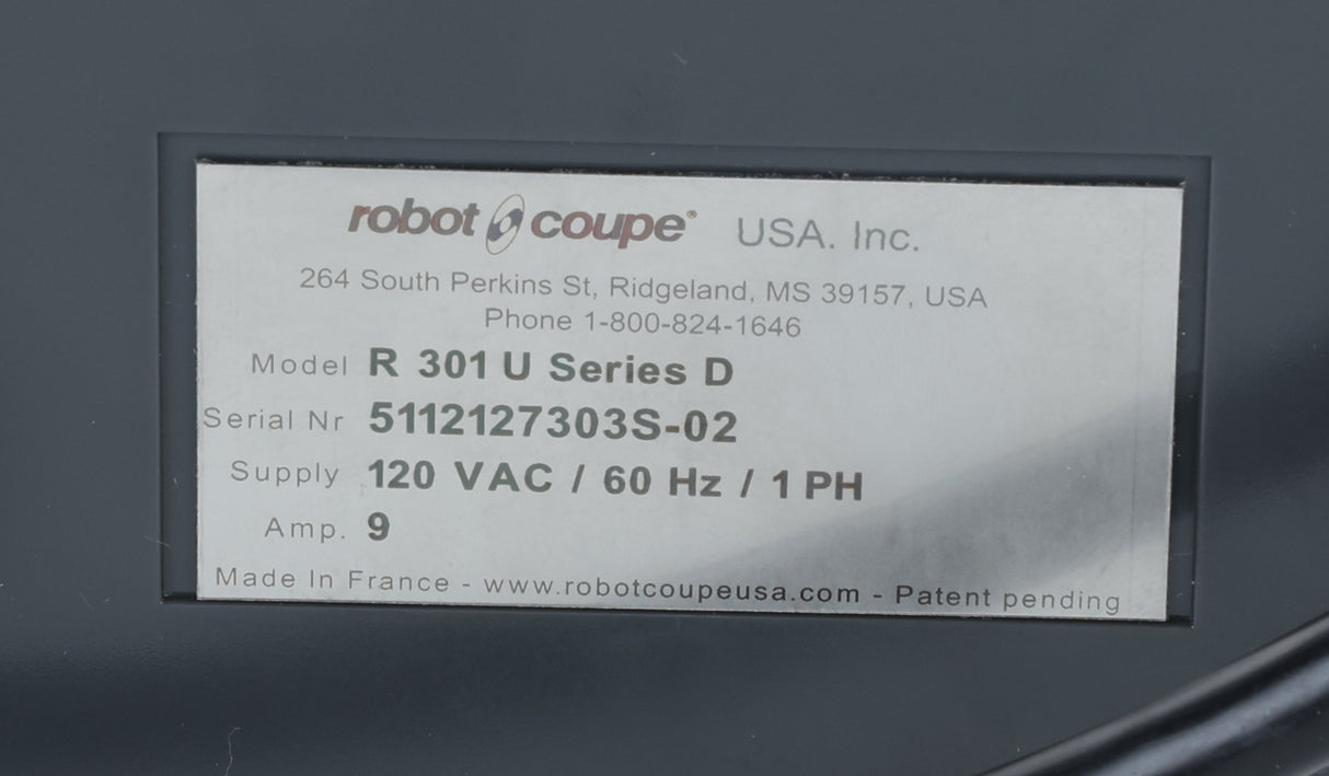 Close-up of a label on a Robot Coupe food processor, showing model R 301 U Series D, serial number 5112127303S-02, supply 120 VAC/60 Hz/1 PH, amp 9. Made in France. Includes company address and contact information at the top. This commercial food processor is designed for reliable use in professional kitchens.