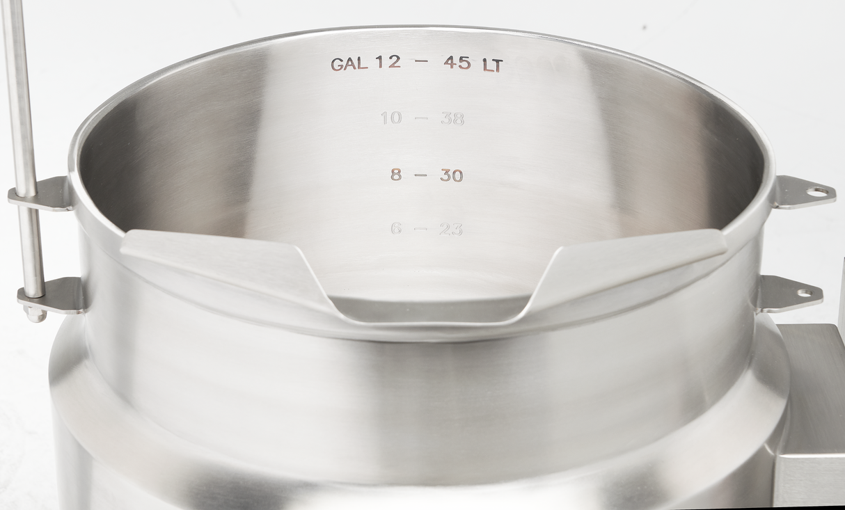 A close-up of a shiny stainless steel tilting kettle with engraved volume markings inside. The measurements, including a 12-gallon capacity, are shown in both gallons (GAL) and liters (LT). The electric kettle is empty.