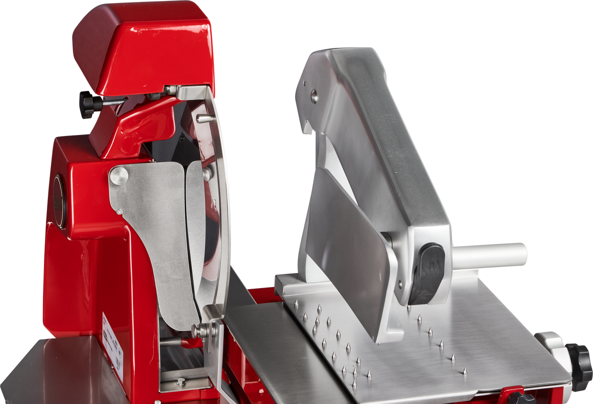 A close-up view of a red and silver Berkel Fly Wheel Slicer with a large, angled chromium-plated carbon steel knife, handle, and safety guards, set on a metallic base. The machine appears clean and is designed for commercial food preparation.