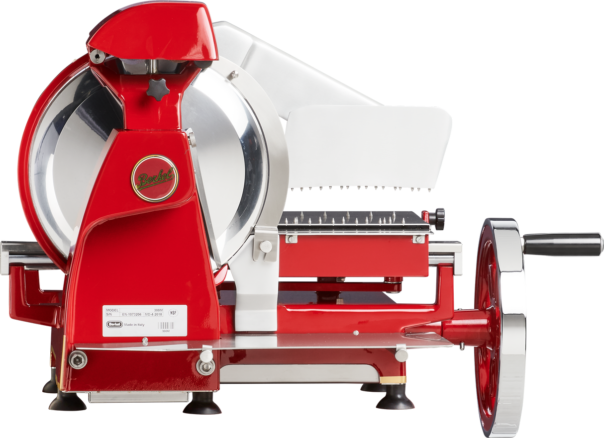 A vintage-style Berkel Fly Wheel Slicer in red and silver, featuring a hand crank, large chromium-plated carbon steel knife, white food tray, shiny finish, exposed mechanisms, four black feet, and the brand logo on the side.
