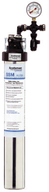 Tall cylindrical water filter assembly with a labeled cartridge at the bottom, black top cap, pressure gauge, and connected piping at the top. The gauge displays pressure, and the “SSM” by ScaleGard is intended for water treatment and antimicrobial protection.