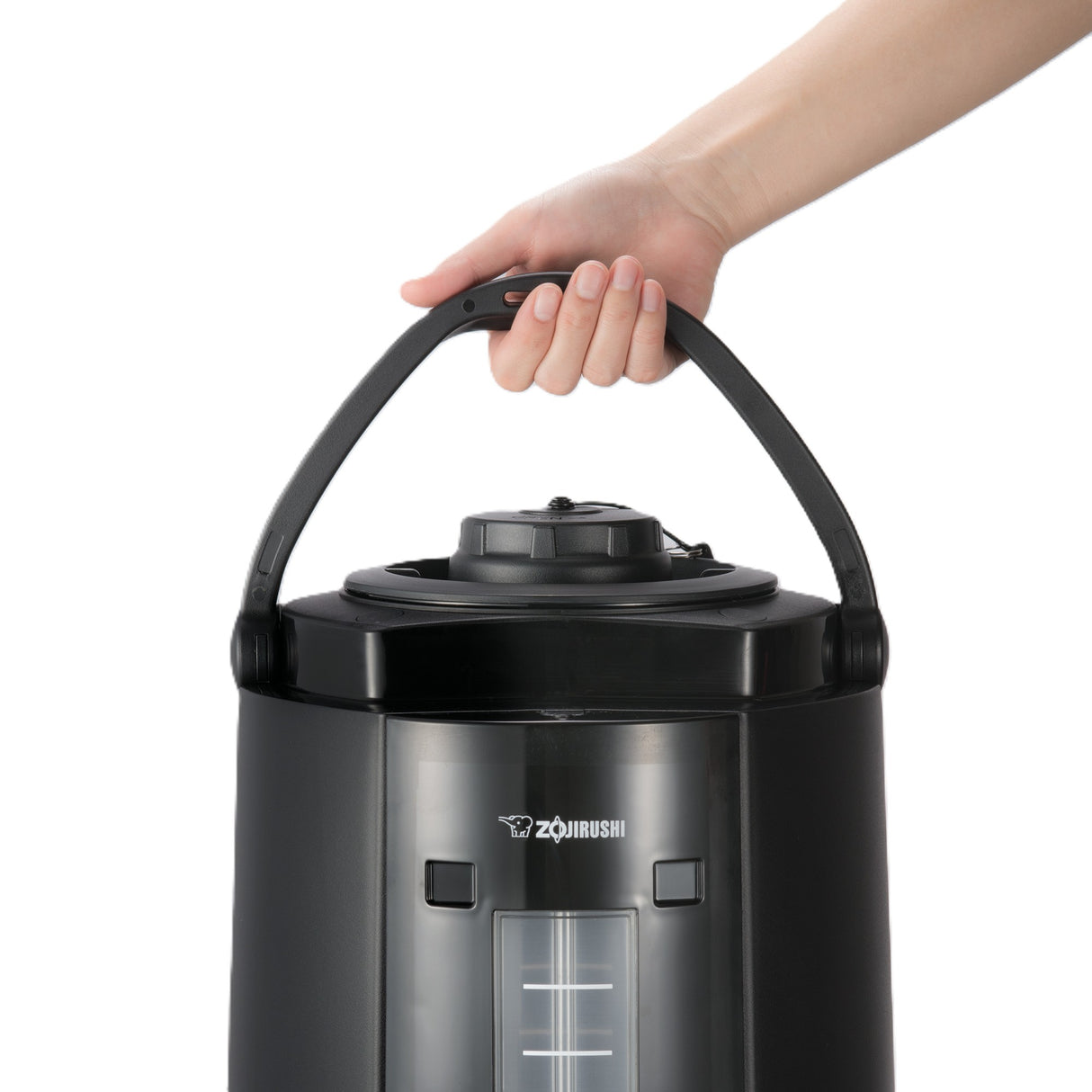 A hand holds the black carrying handle of a large Zojirushi beverage dispenser with an insulated stainless steel vacuum liner, transparent water level window, and round lid, against a white background.
