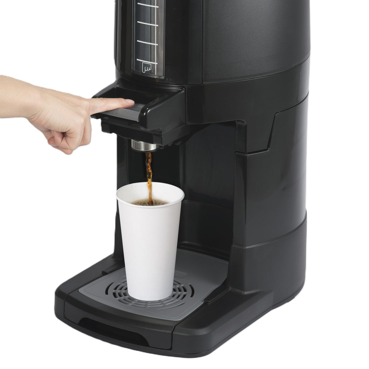 A hand presses a lever on a large insulated beverage dispenser, pouring coffee into a white paper cup placed on the built-in tray. The dispenser features a tall, clear measurement window and a stainless steel vacuum liner to retain heat.