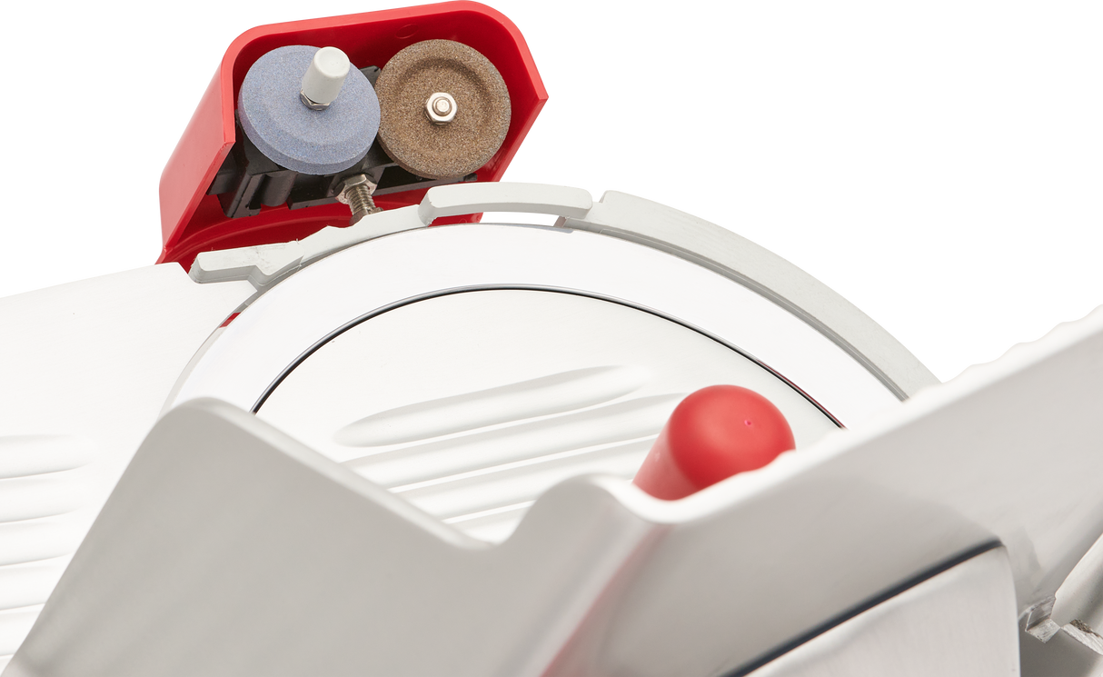 Close-up view of a Berkel slicer, highlighting the 12 inch carbon steel knife, guard, and two sharpening wheels—one blue, one brown—in a red holder above the blade. The manual gravity feed slicer has a metallic and white finish with a red safety handle in front.