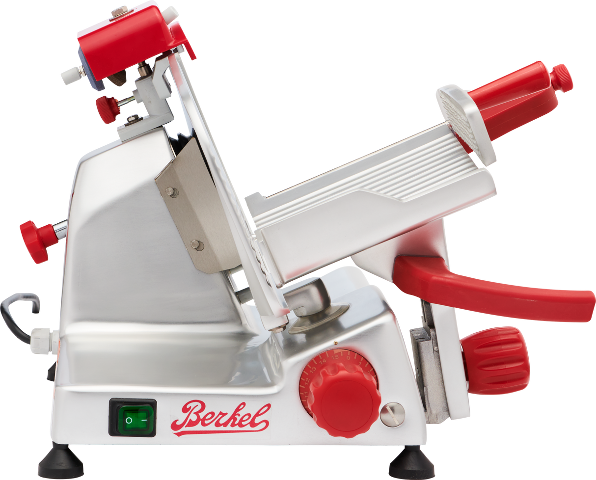 A stainless steel Berkel gravity feed slicer with red knobs and handles, a tilted adjustable platform, and a sharp circular blade. The machine has an on/off switch and the Berkel logo in red. Its overall design is modern and industrial.