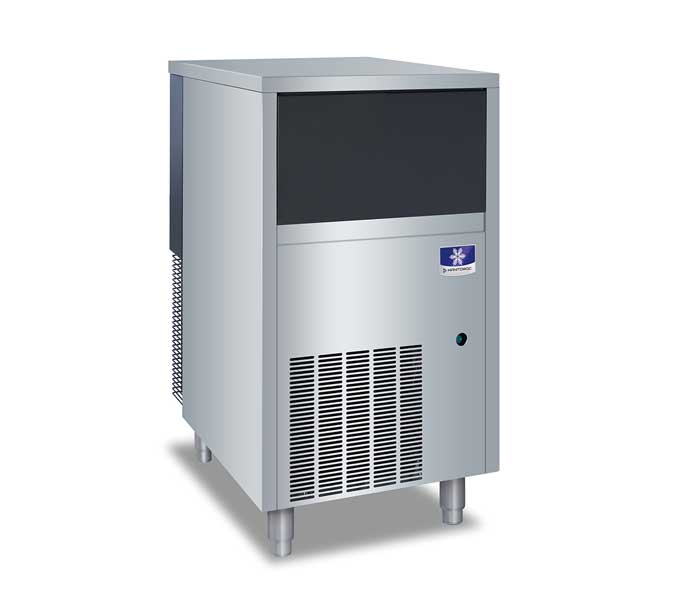 A commercial Manitowoc ice maker stands on four legs with a sleek, industrial design. The upper section has a black panel, while the lower portion features a vented grille and a small blue logo near the top right.