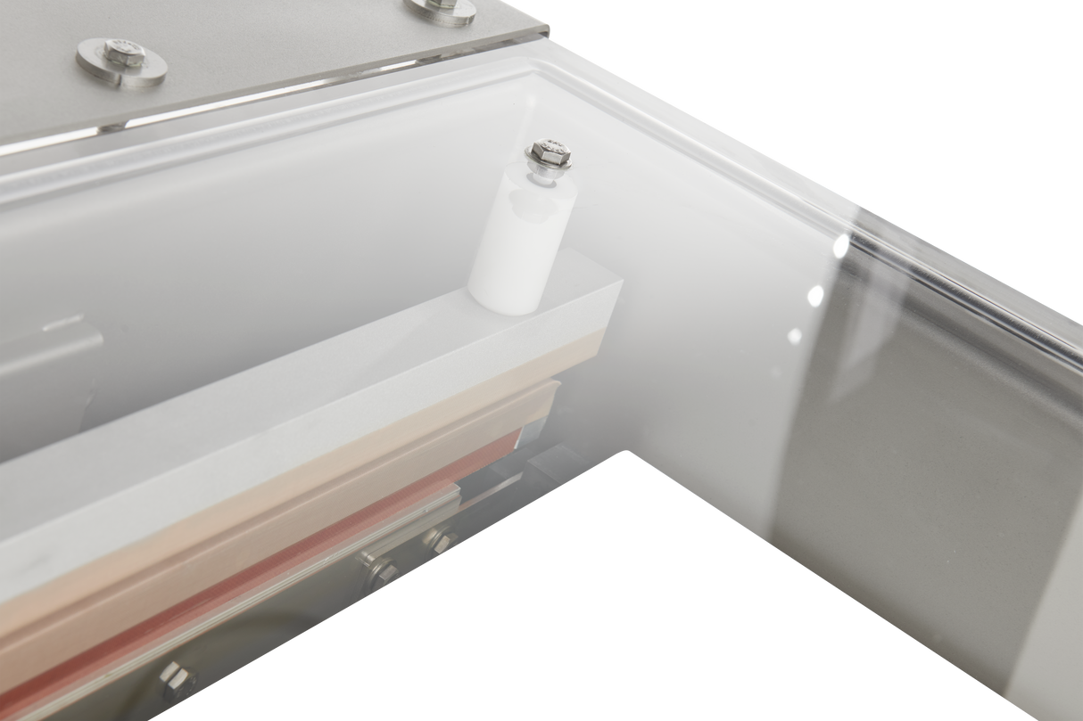 Close-up of a Berkel Vacuum Packaging Machine component, featuring a frosted transparent cover, white cylindrical piece with a bolt on top, metal bolts, beige and pale gold bars, and reflections on the smooth surfaces of its single chamber.