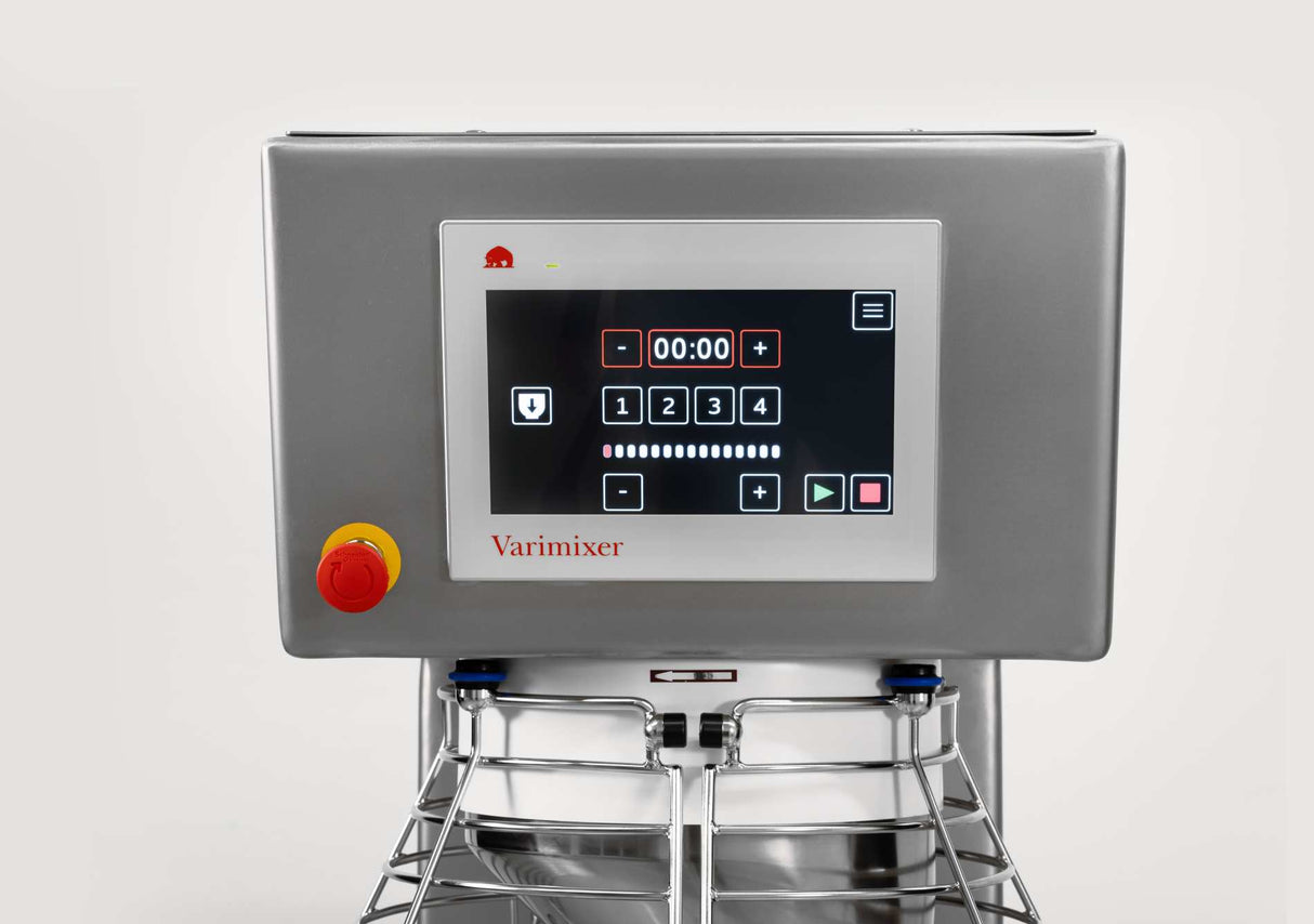 A close-up of a Varimixer planetary mixer control panel featuring a touchscreen display with a digital timer, numeric keypad, and various control icons. A large red emergency stop button is on the left. The panel has a stainless steel finish.