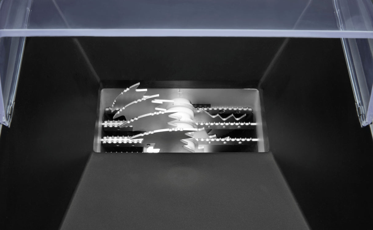 Close-up of an industrial Ice Crusher’s blades, seen from above. Multiple sharp, interlocking, jagged metal teeth are visible inside a black and silver encasement, with a partially transparent plastic lid at the top of the image.