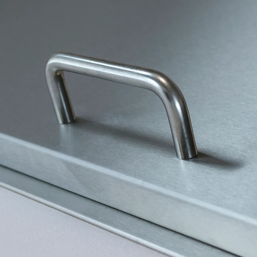A close-up view of a rectangular metal surface on a refrigerated sandwich prep table with a simple, curved silvery handle attached. The handle is slightly rounded and mounted on the flat, brushed surface. The background is out of focus.