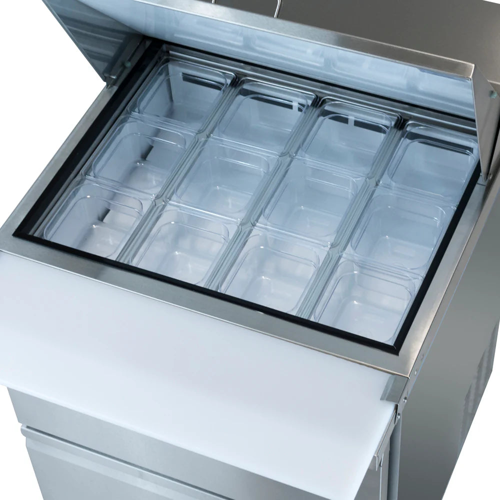 A top-down view of a stainless steel mega top prep table with its lid open, revealing twelve empty, clear plastic food pans in a 3x4 grid inside a refrigerated compartment. A white cutting board is attached to the front.