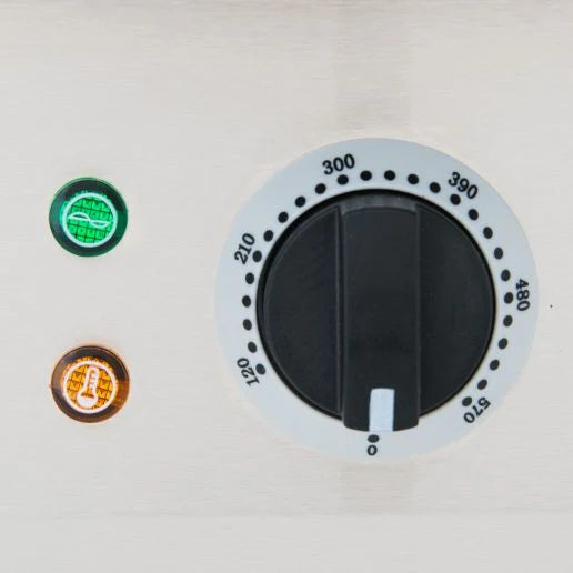 A close-up of an Empura griddle’s temperature control knob on a metallic panel, marked from 0 to 570 degrees. Two indicator lights sit to the left: the top green, the bottom orange—both feature clear symbols inside this stainless steel griddle.