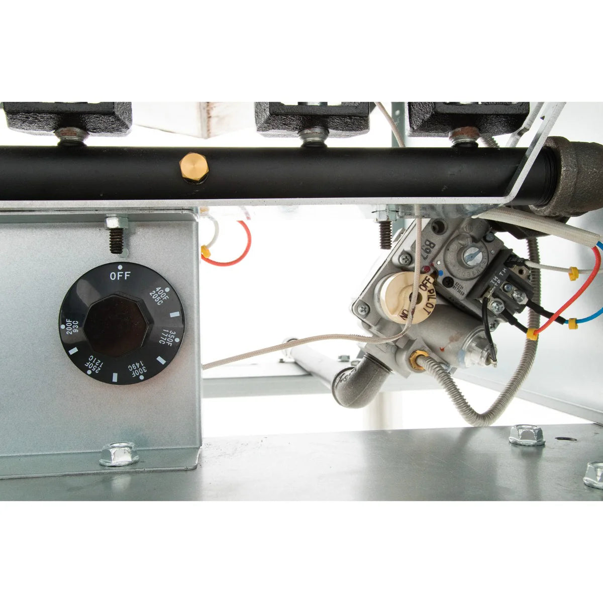 Close-up view of a gas fryer control valve and thermostat dial, marked with OFF, temperature settings, and various numbers. Wires and metal pipes connect to the mechanism on a commercial fryer with visible bolts and fittings.