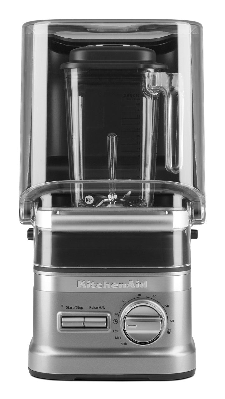 A silver KitchenAid Commercial Blender with a clear plastic sound enclosure, 60 oz. capacity pitcher, and black lid. The base offers control buttons, a large speed dial, and the KitchenAid logo. The image is taken from the front against a white background.