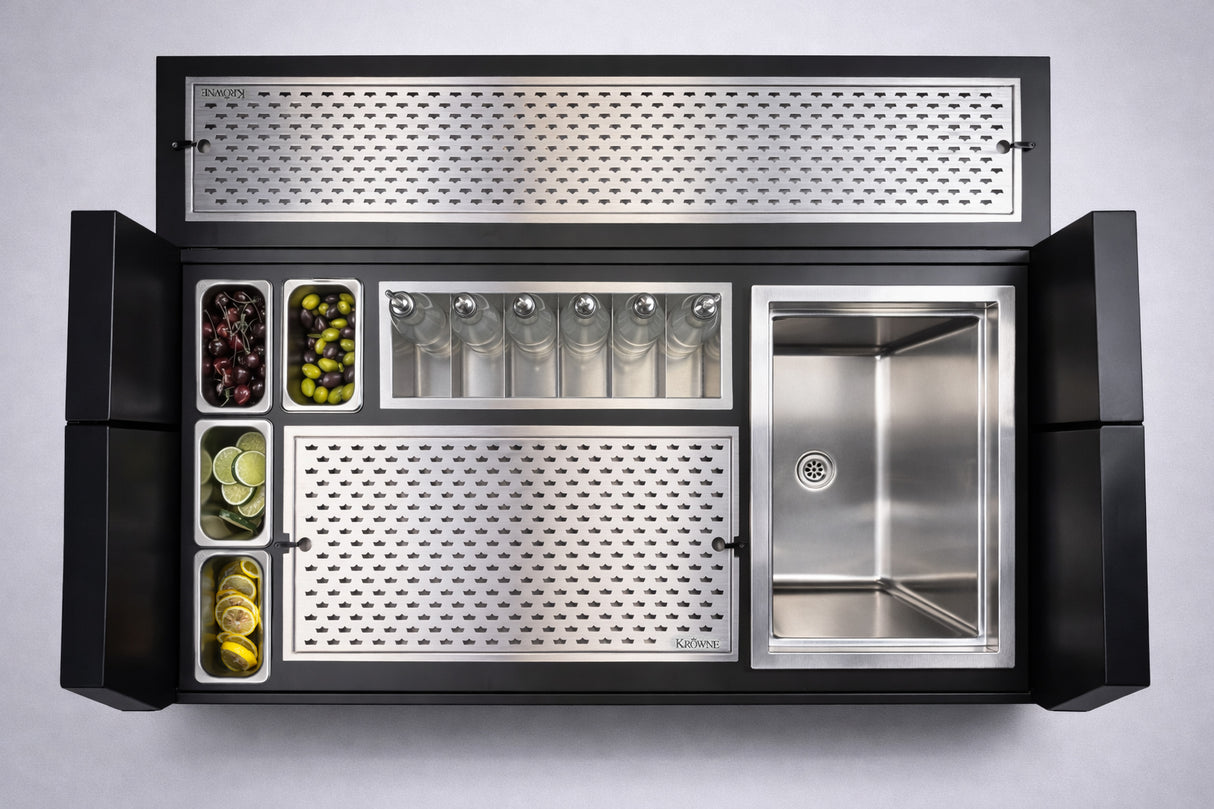 A top-down view of a sleek, modern bar station with a stainless steel sink, six glass bottles, metal containers of garnishes, and an insulated ice bin. The NomadBar Mobile features perforated metal panels in a black frame against a light background.